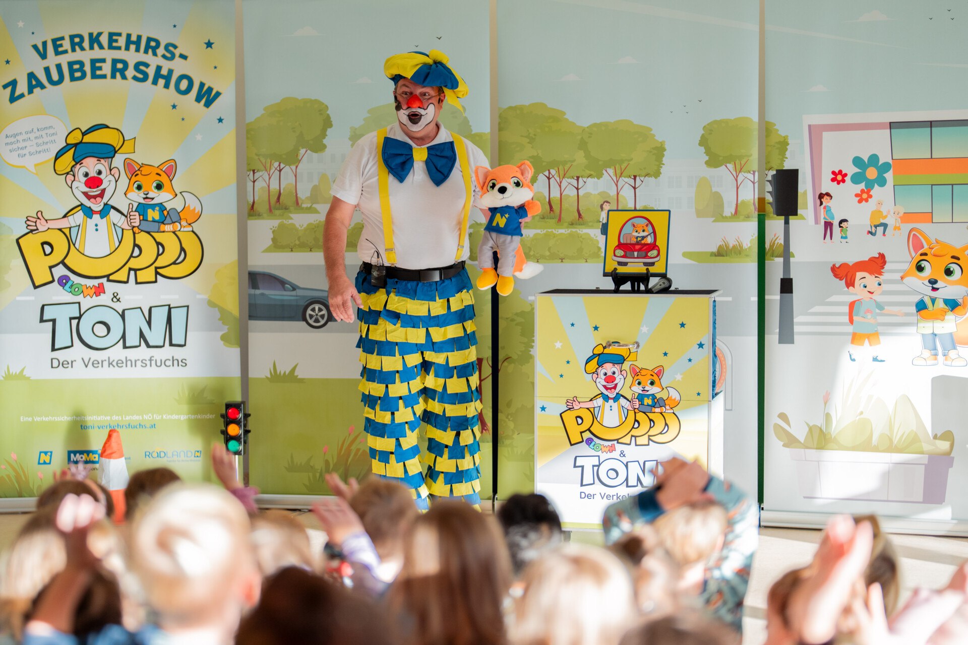 Clown mit Fuchshandpuppe auf der Bühne vor vielen Kindern