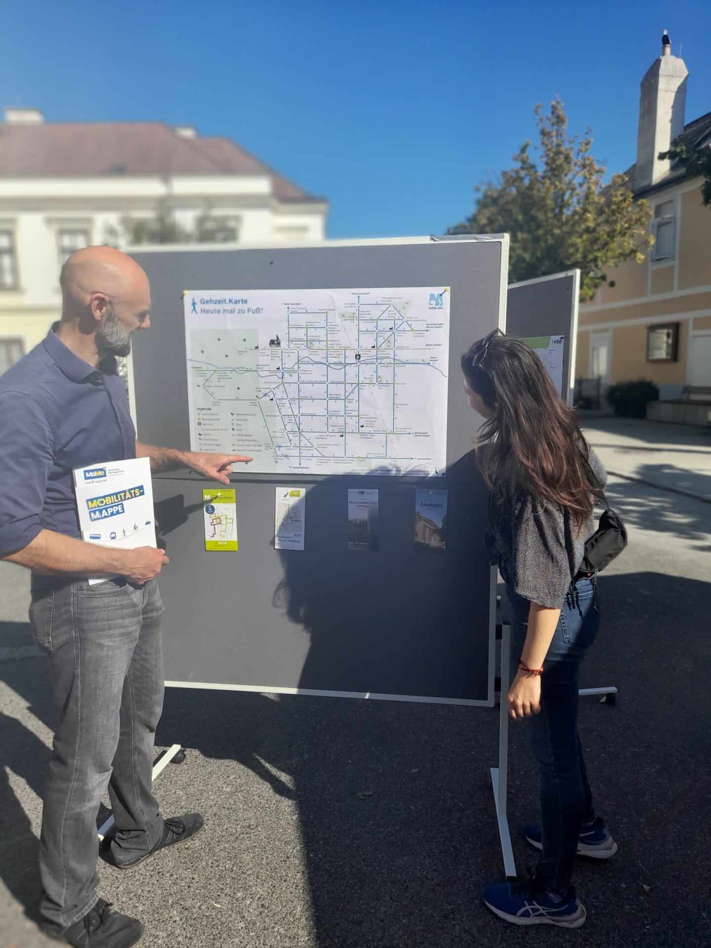 Personen stehen vor Pinnwand mit Gehzeit.Karte und Mobilitätsmappe in der Hand