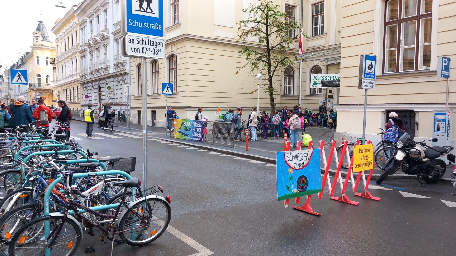 Straße mit Scherengitter vor Schule abgesperrt mit vielen Kindern auf der Straße