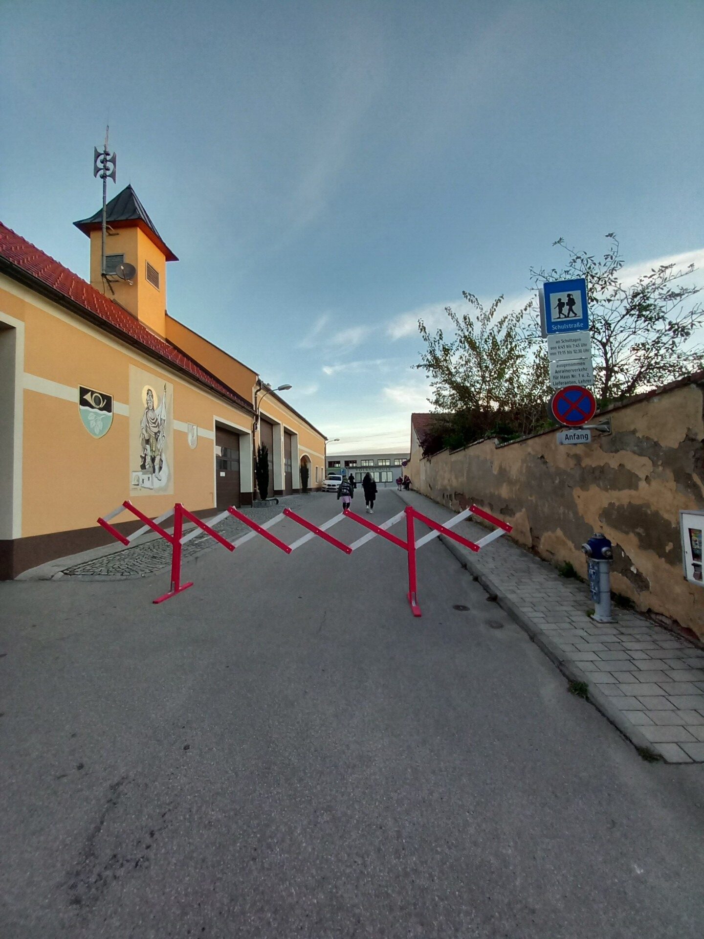 Schulstraße mit Scherengitter und Volksschule im Hintergrund