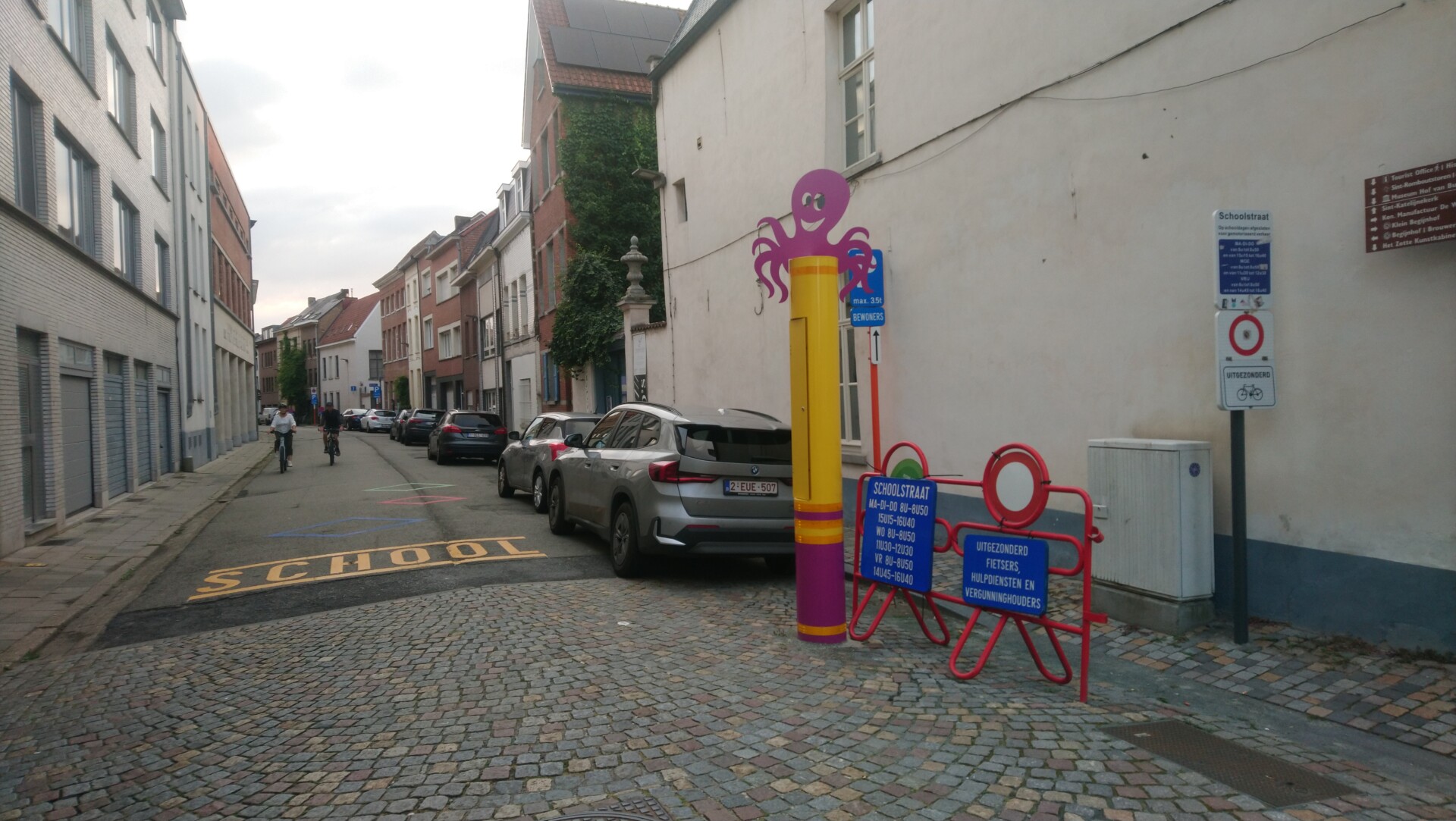 Schulstraße mit Scherengitter seitlich, Schulstraßenschild und Lila gelber Säule