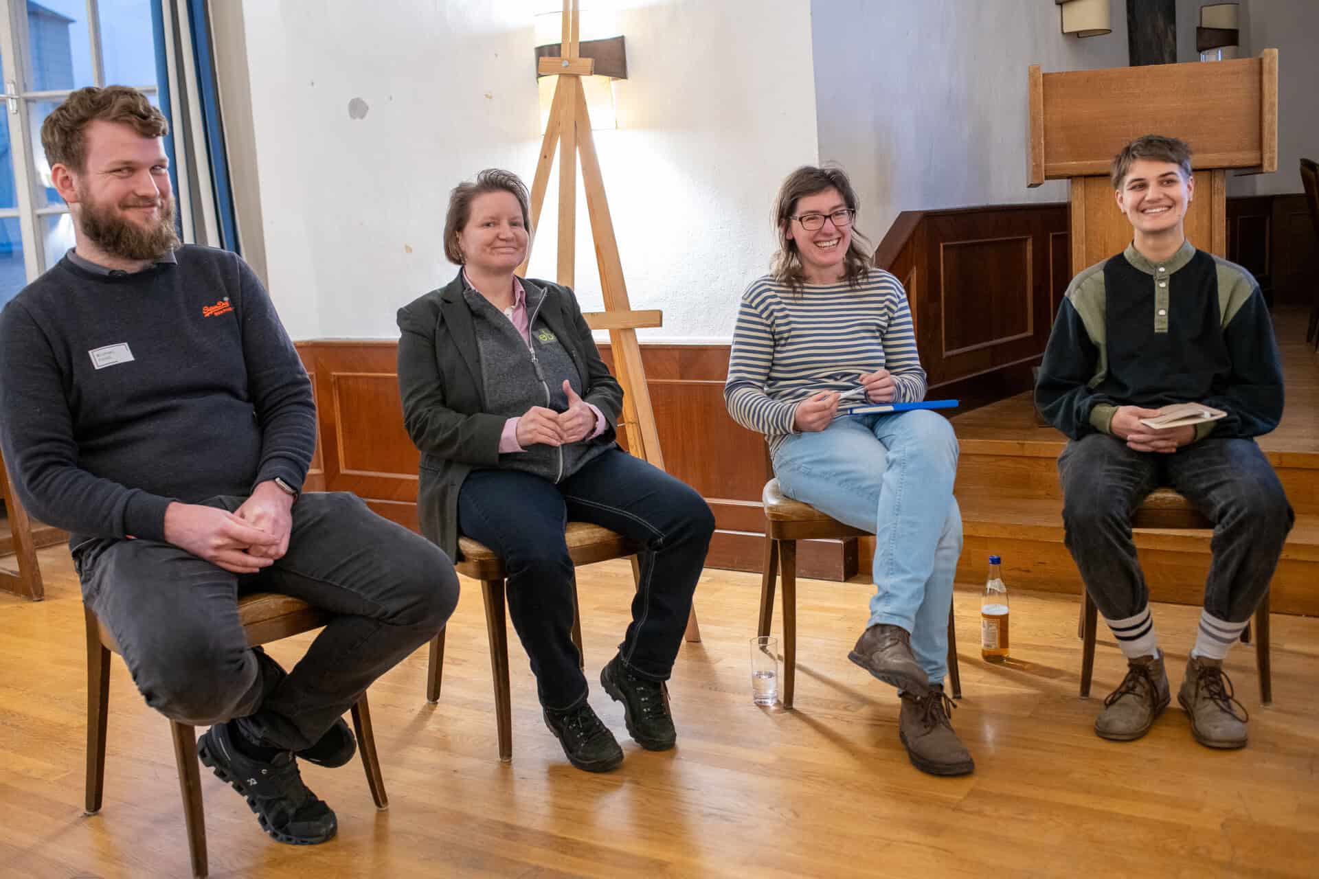 Vier Personen sitzen nebeneinander und lachen ins Bild