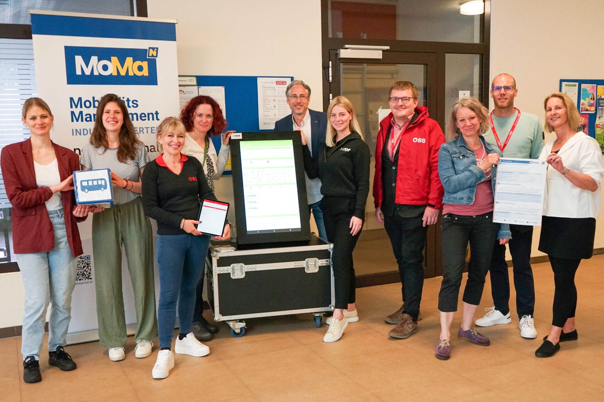 Menschen stehen zum Gruppenfoto aufgereiht mit Unterlagen und Rollup zur Veranstaltung.