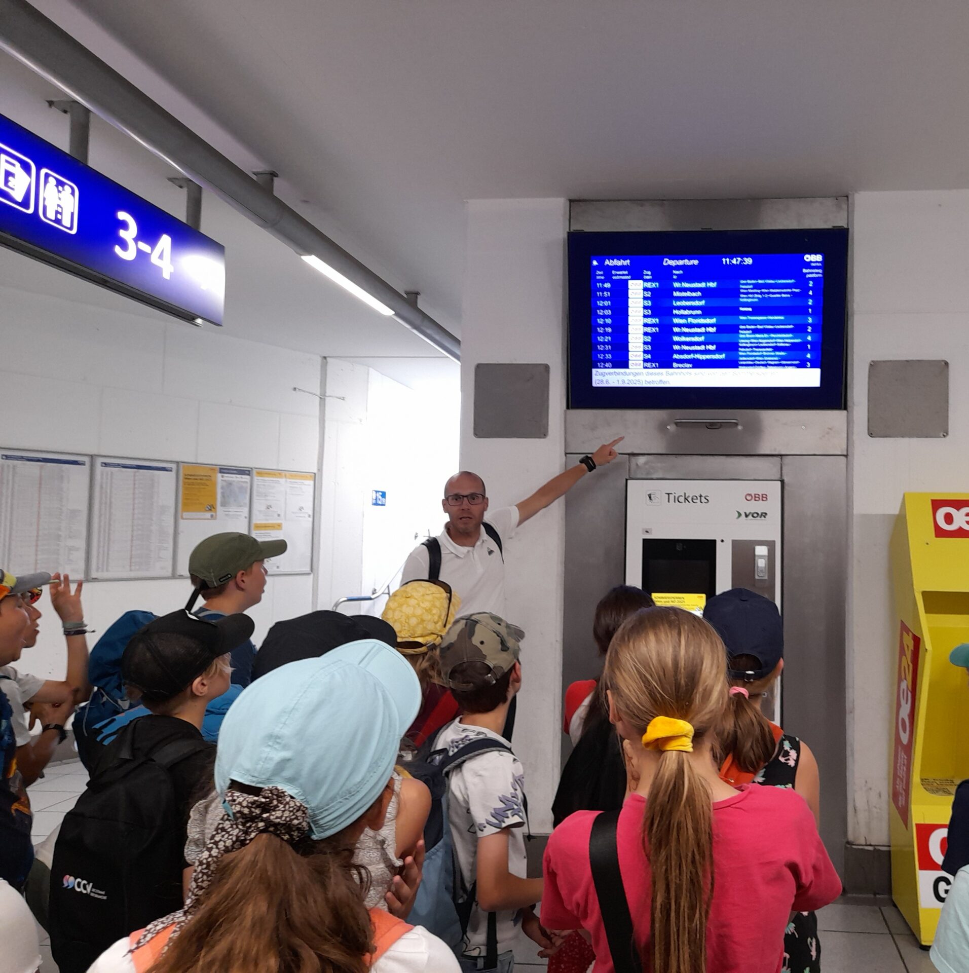 Mann erklärt Kinder die Anzeigetafel am Bahnhof Mödling