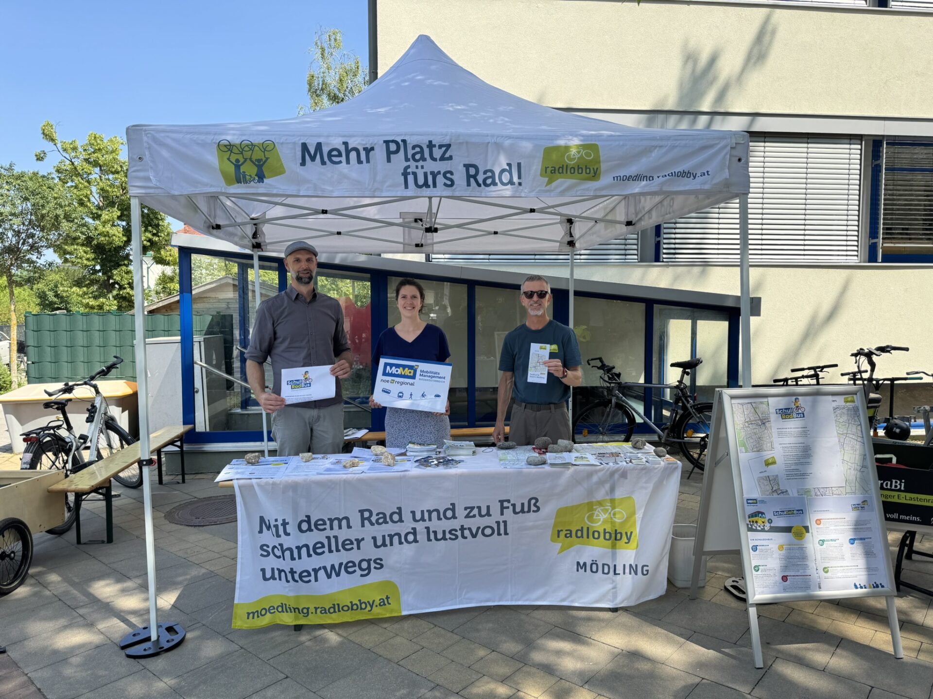 Drei Menschen stehen unter einem Zelt mit Infostand zur Radlobby und dem Projekt SchulRadBus