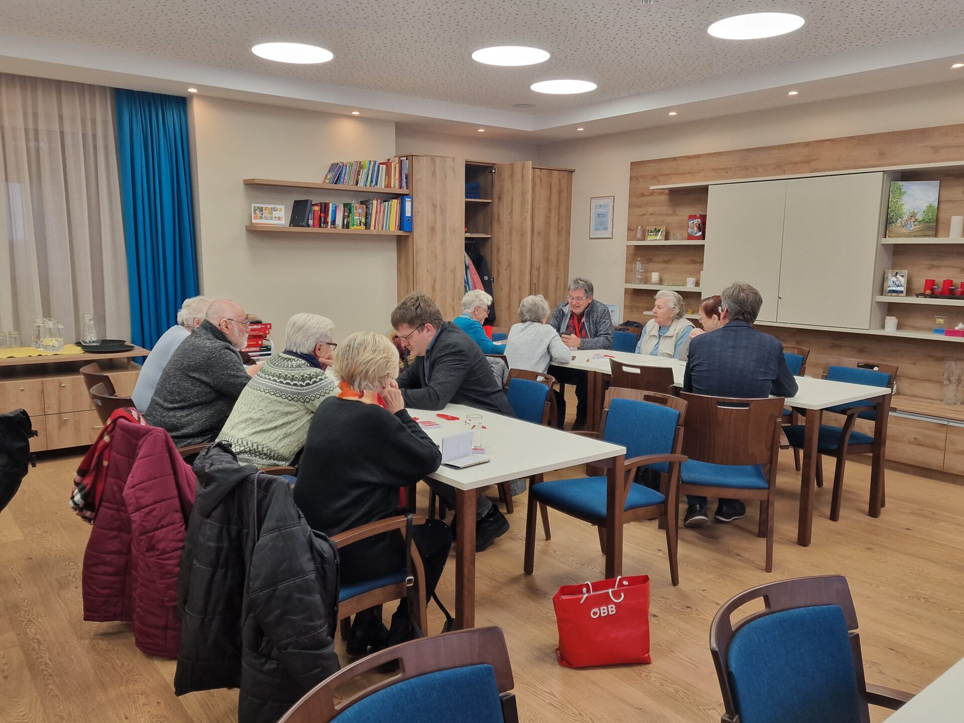 Ältere Menschen sitzen an Tischen und lassen sich ÖBB App erklären.