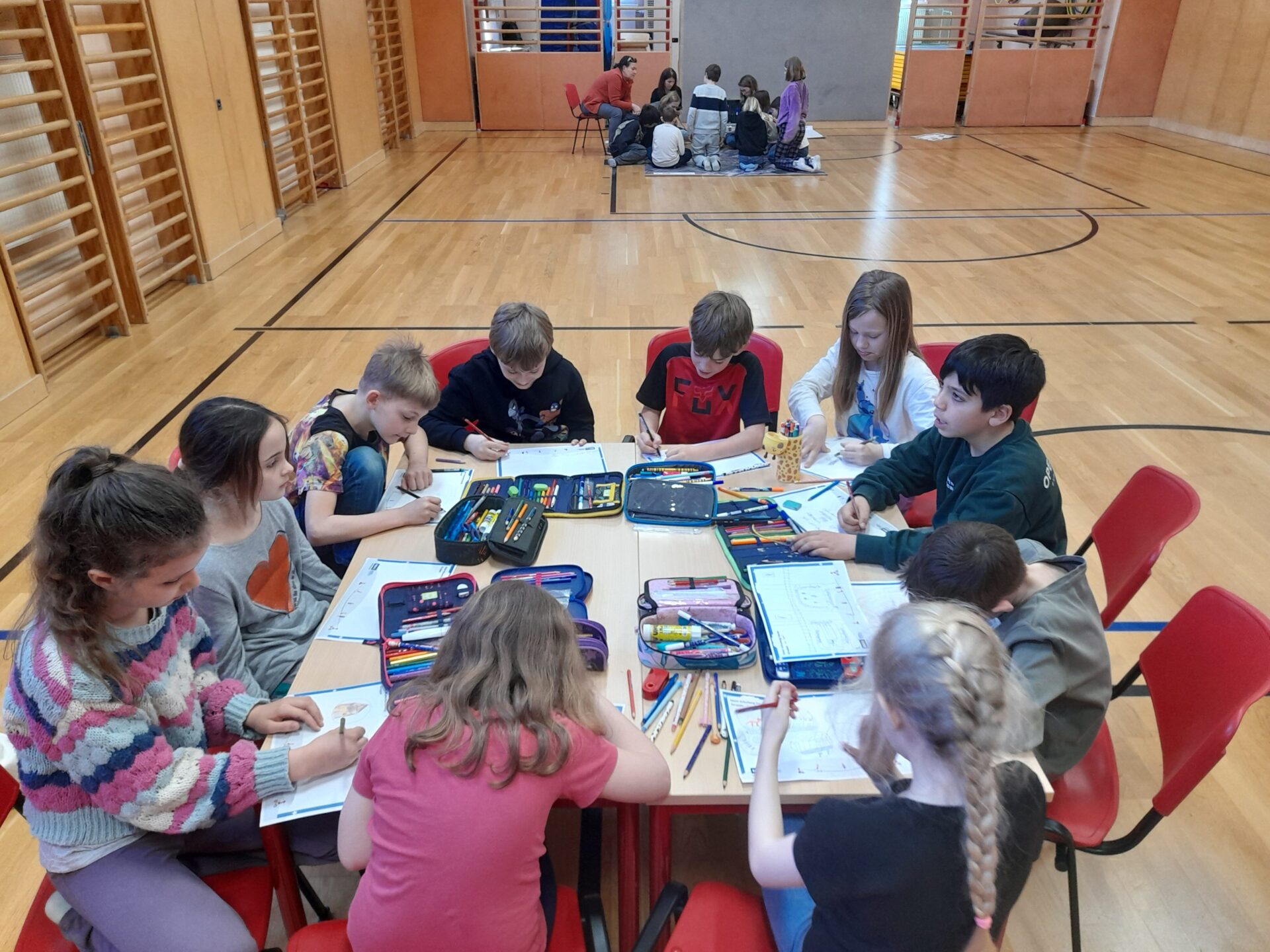 Kinder sitzen um einen Tisch und zeichnen ihren Schulweg.